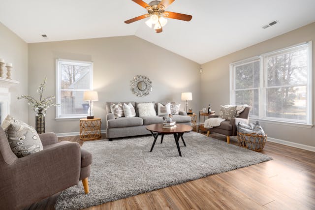 A furnished living room with a gray rug a couch and two chairs